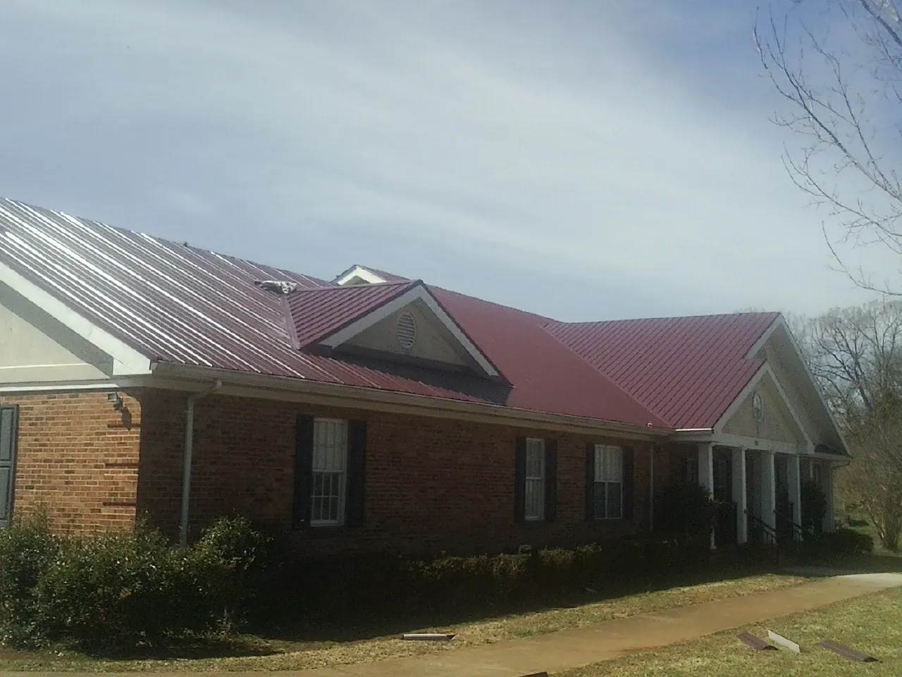 Red metal roof with gabled entries on a long brick building, from a Hail Damage Roof Repair job in Watervliet
