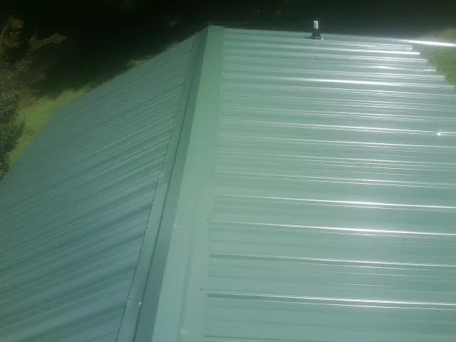 New green metal panels meeting at the ridge of a roof — Flat Roof Repair work by our crew in Watervliet