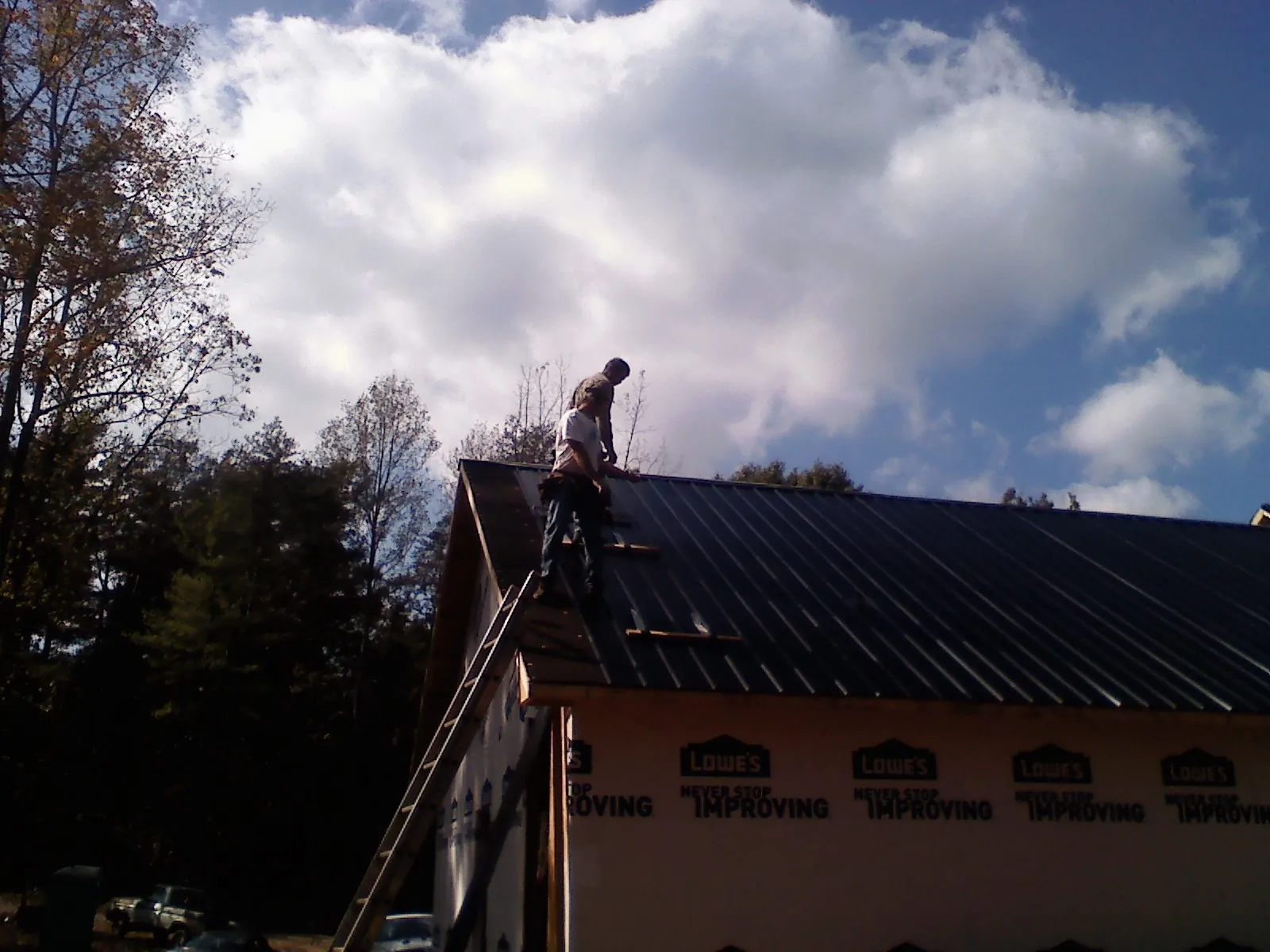 Roofer fastening dark metal panels high against a cloudy sky, from a Roof Inspection job in Watervliet