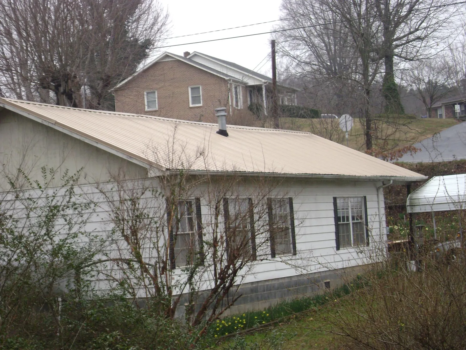 Tan metal roof on a white sided house set into a hillside — Commercial Roofing by Roofing Brothers in Watervliet